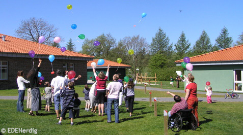 Eine Gruppe Menschen mit Handicap und ohne laesst Luftballons steigen