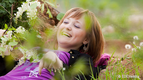 Frau mit Handicap liegt laechelnd zwischen Wildblumen