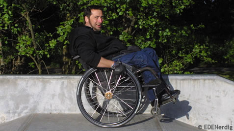 Mann im Rollstuhl fährt grinsend auf nur zwei Raedern